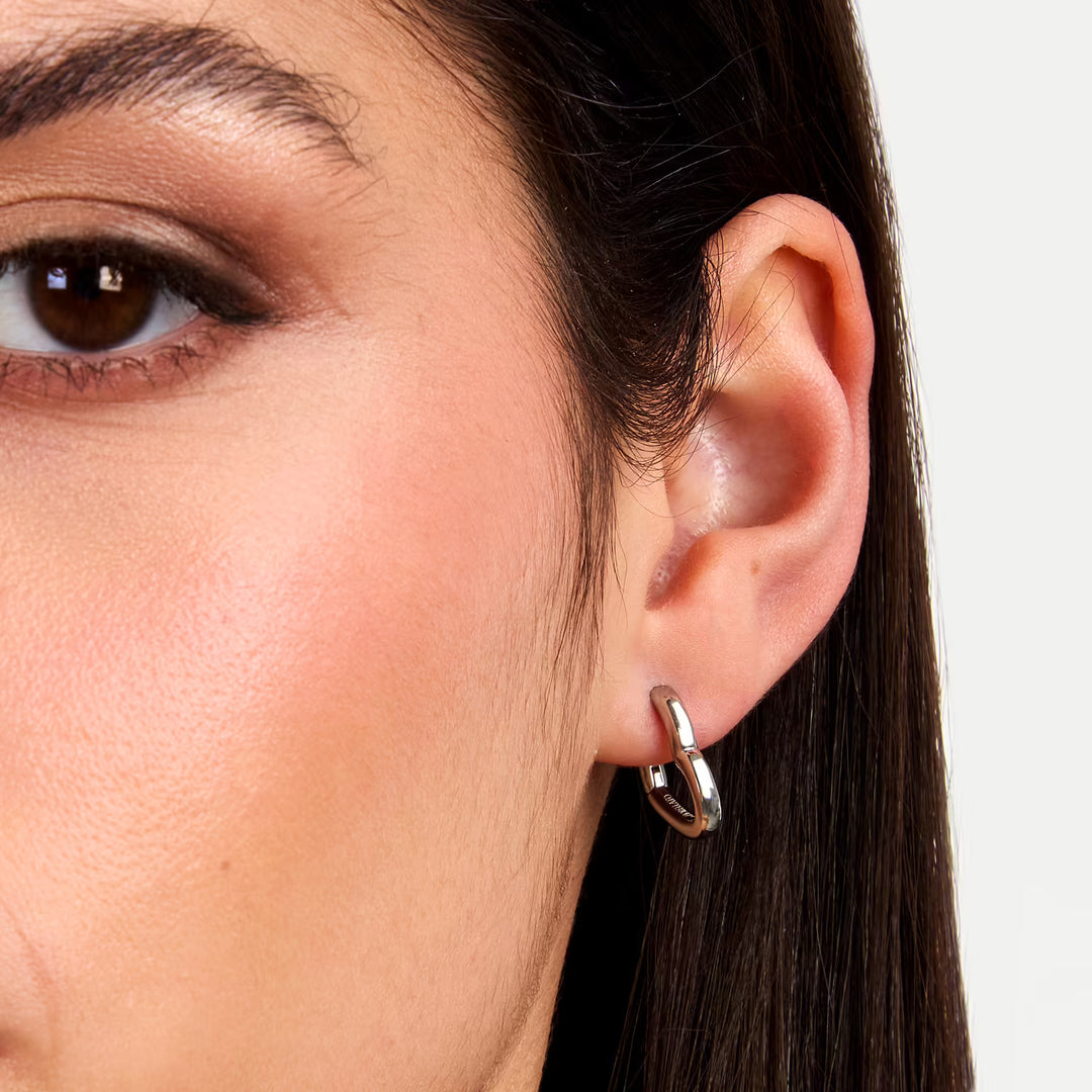 Близък план на ухото с обеца крийол „сърце“ от неръждаема стомана, сребриста.