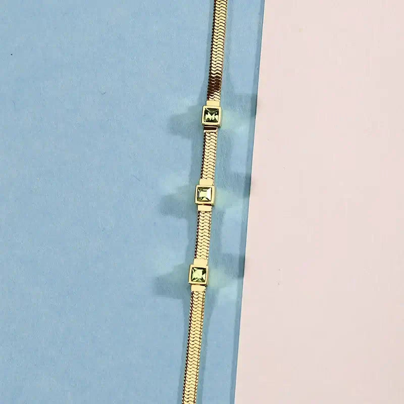 Лайфстайл кадър на гривна със зелени квадратни циркони върху цветен фон.
