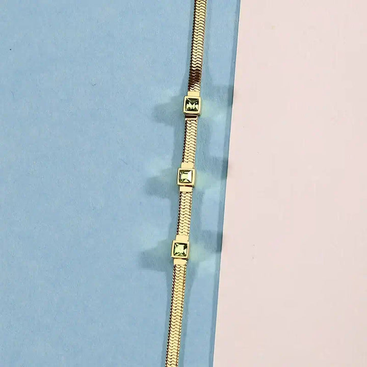 Лайфстайл кадър на гривна със зелени квадратни циркони върху цветен фон.
