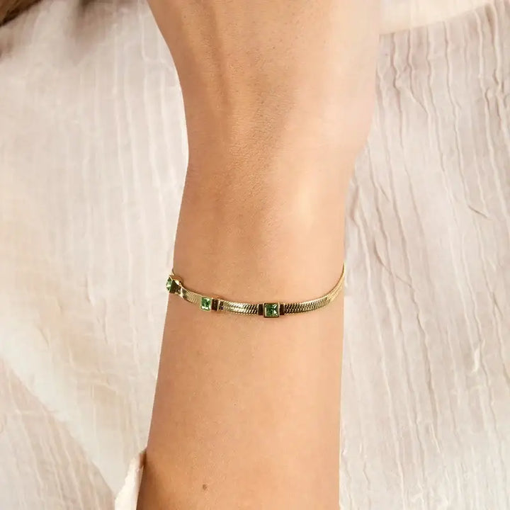 Близък план на златиста гривна със зелени циркони 3×3 мм на китка.

