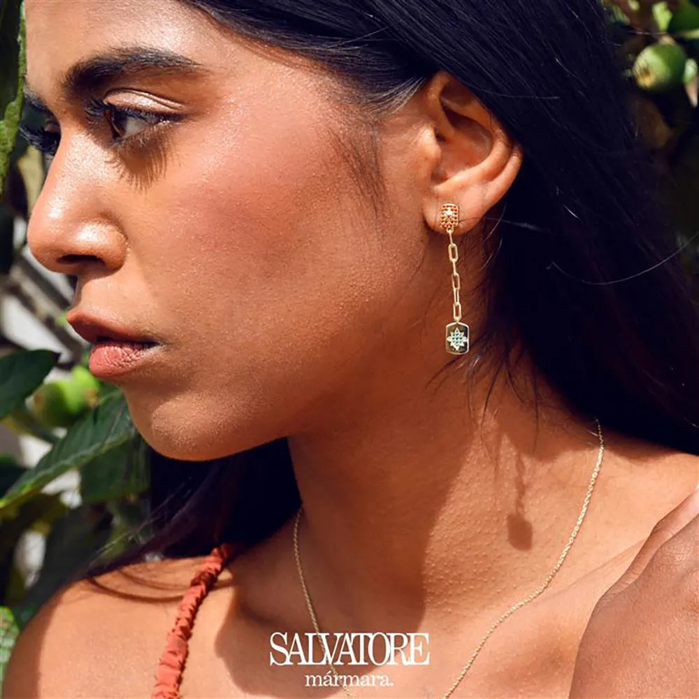 Модел носи дълги сребърни обеци Salvatore Plata с параиба циркон и златиста верижка, на фона на зелени листа.