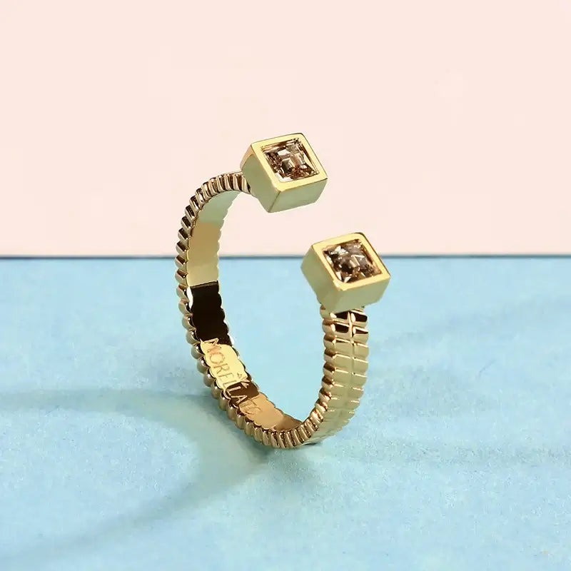 Близък план на отворен позлатен пръстен с два квадратни циркона на длан.