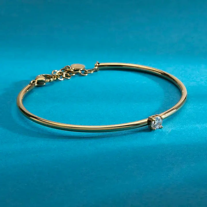 Позлатена твърда гривна с бял циркон върху китка на модел, портрет.