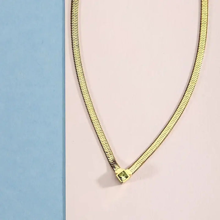 Колие със златиста „snake“ верижка и централно квадратно камъче, студио.
