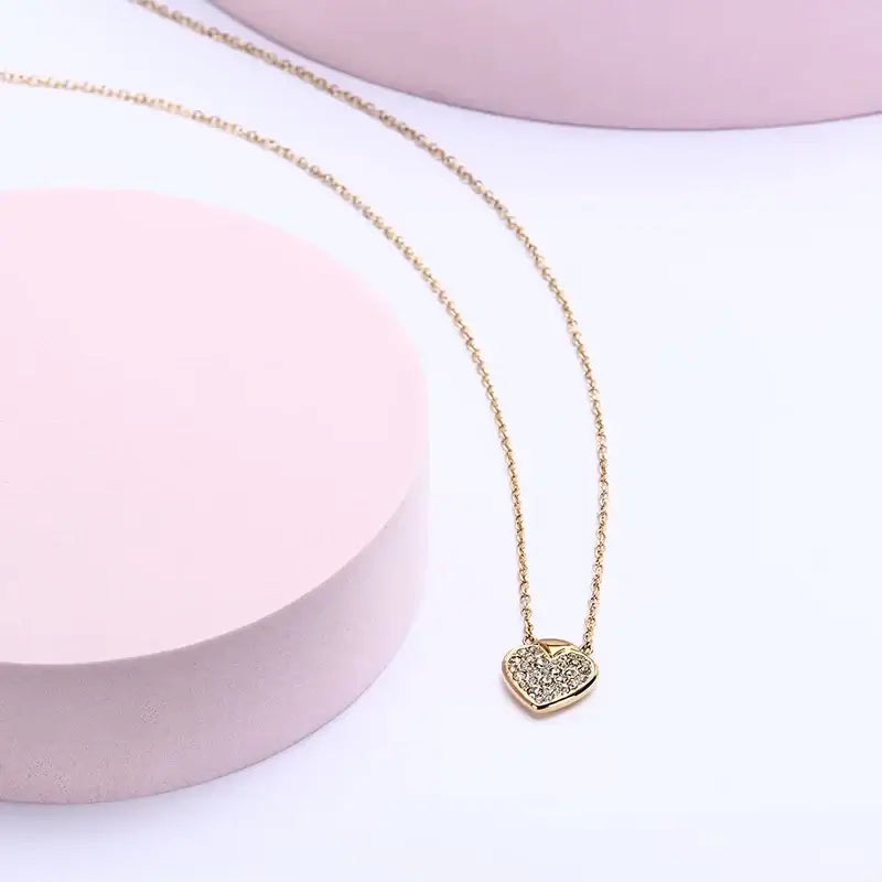 Лайфстайл кадър на позлатено колие сърце с кристали върху розов фон.