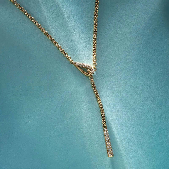 Лайфстайл кадър на позлатено Y-колие с бели кристали на светлосин фон.