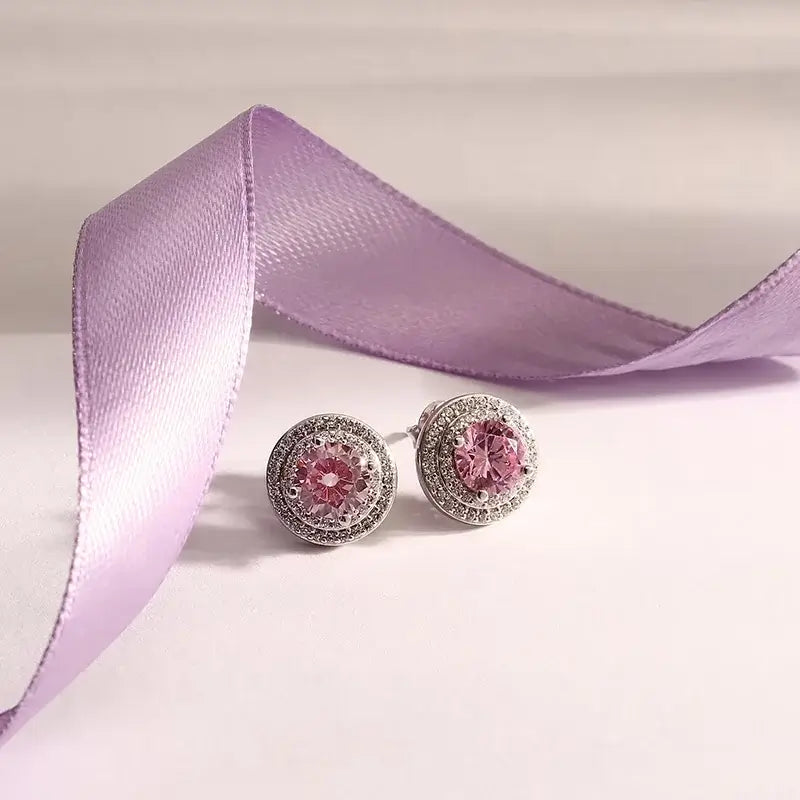 Лайфстайл кадър на сребърни обеци „ореол“ с розов циркон върху фон с лилава лента.