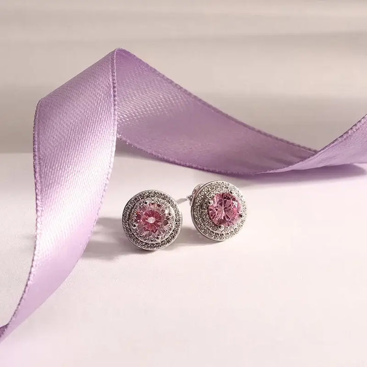 Лайфстайл кадър на сребърни обеци „ореол“ с розов циркон върху фон с лилава лента.