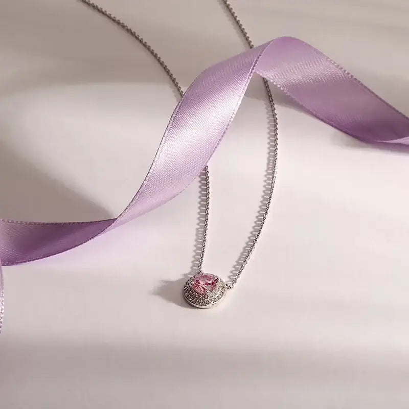 Лайфстайл кадър на сребърно колие 925 с розов централeн циркон върху фон с лилава лента.