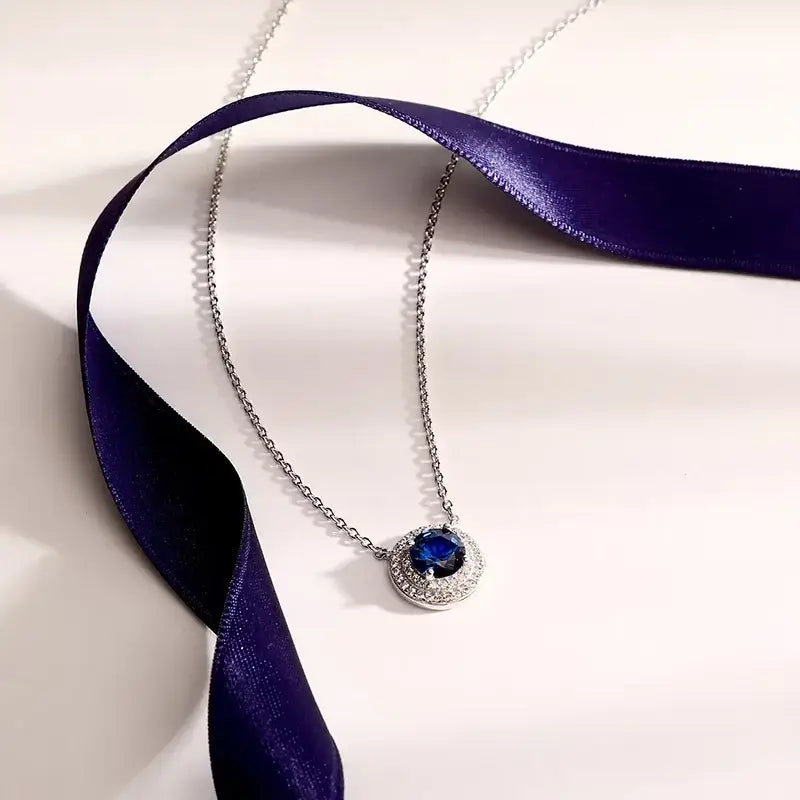 Лайфстайл кадър на сребърно колие със син център върху светъл фон с лилава лента.