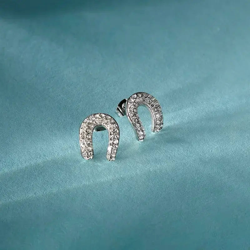 Лайфстайл кадър на сребристи обеци „подкова“ с кристали върху светлосин фон.