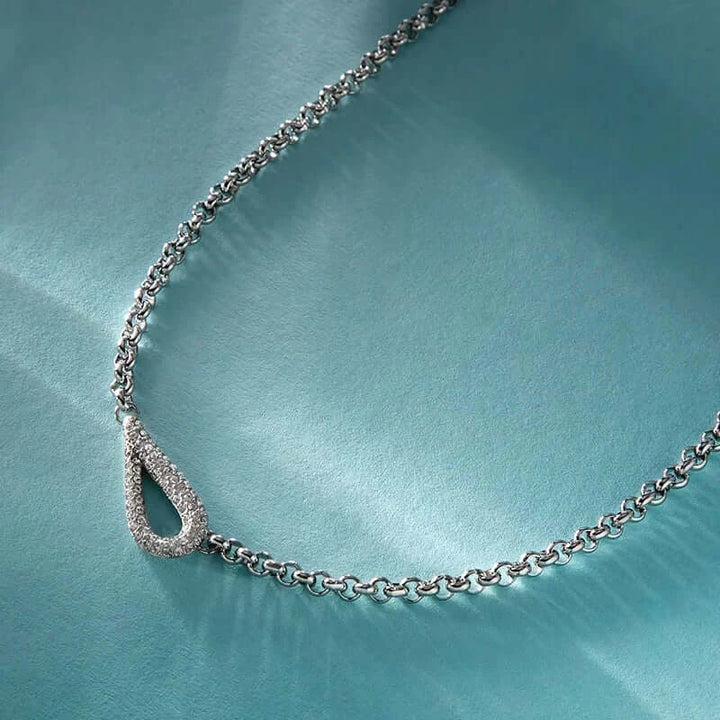 Лайфстайл кадър на сребристо колие с висулка „капка“ върху светлосин фон.